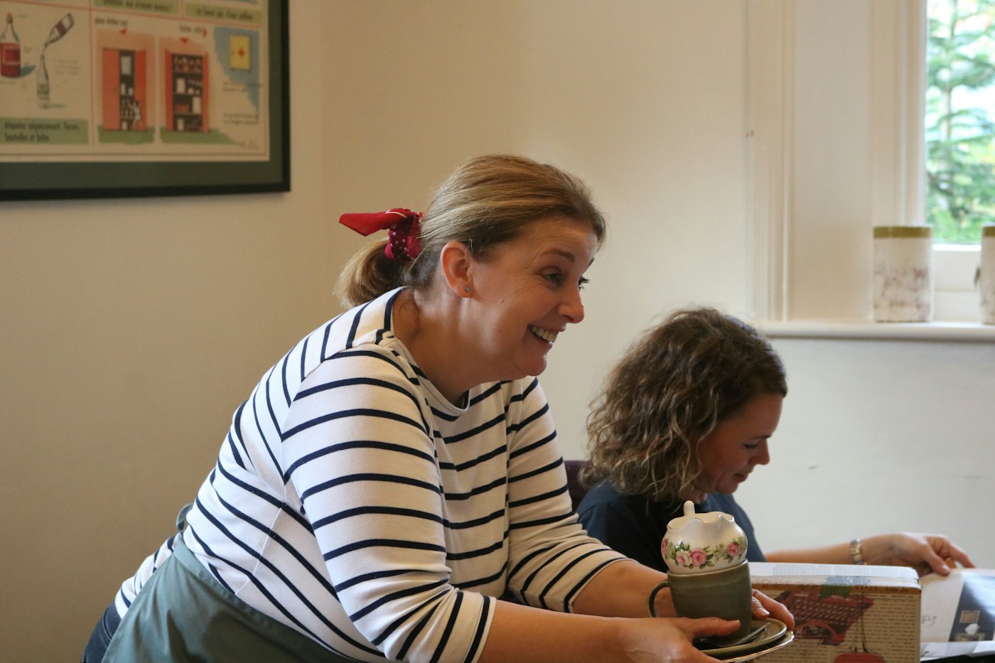 A smiling woman in a striped top serving tea in a ceramic cup