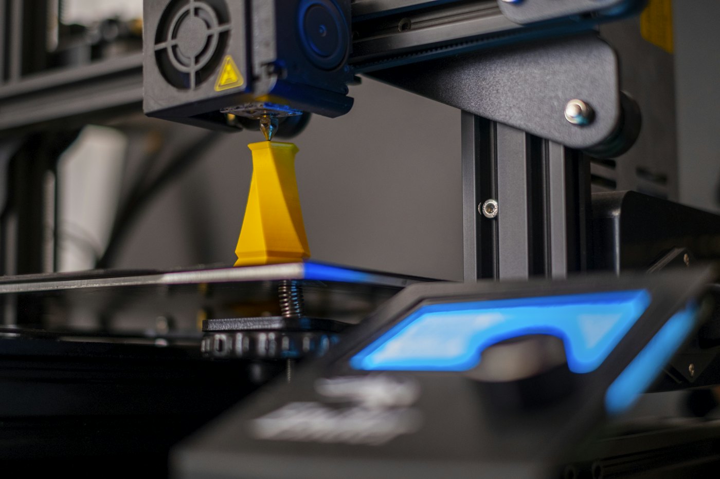 Close-up of a 3D printer nozzle lit in blue